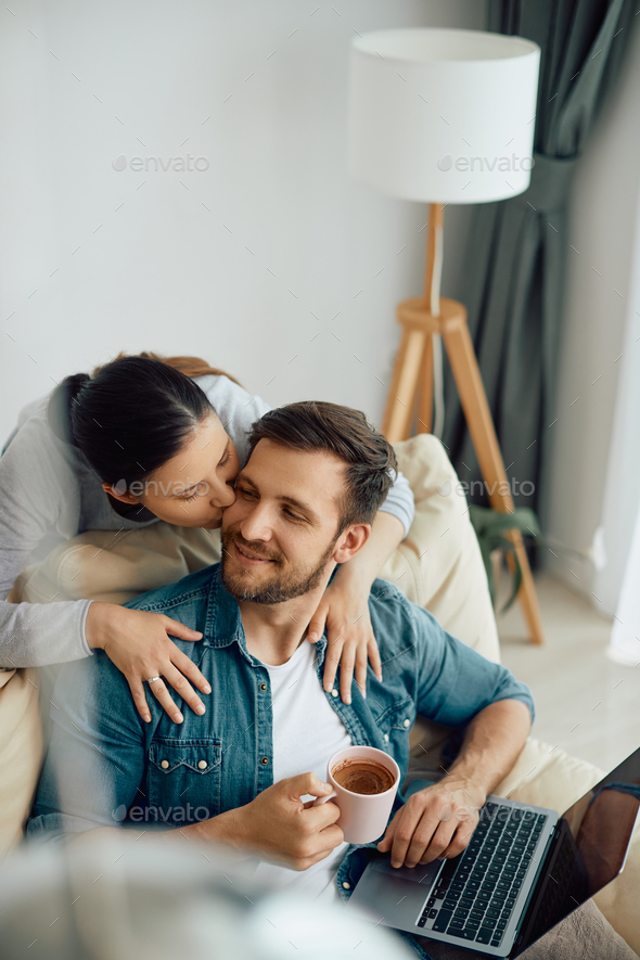 Affectionate Woman Kissing Her Husband While He Is Drinking Coffee And